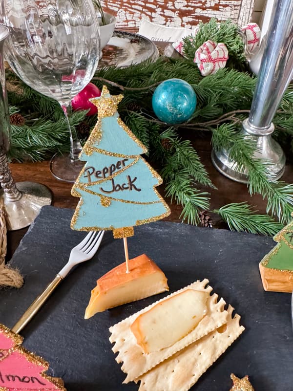 Blue Wood Christmas Tree Cheese Marker on cheese with crackers. 
 Easy to make DIY Cheese Markers using Dollar Tree Supplies for Customized Appetizer Markers