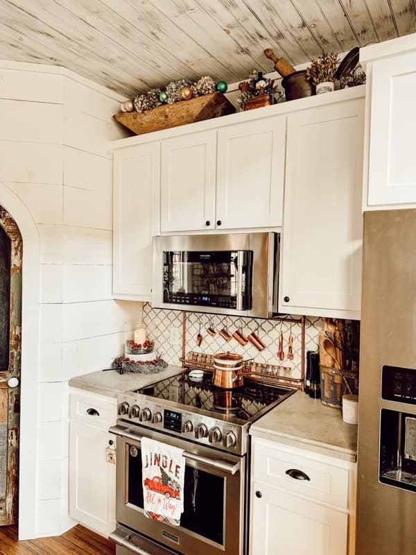 Kitchen above cabinets decorated for Christmas with vintage dough bowl filled with dried hydrangeas and vintage Christmas ornaments.  