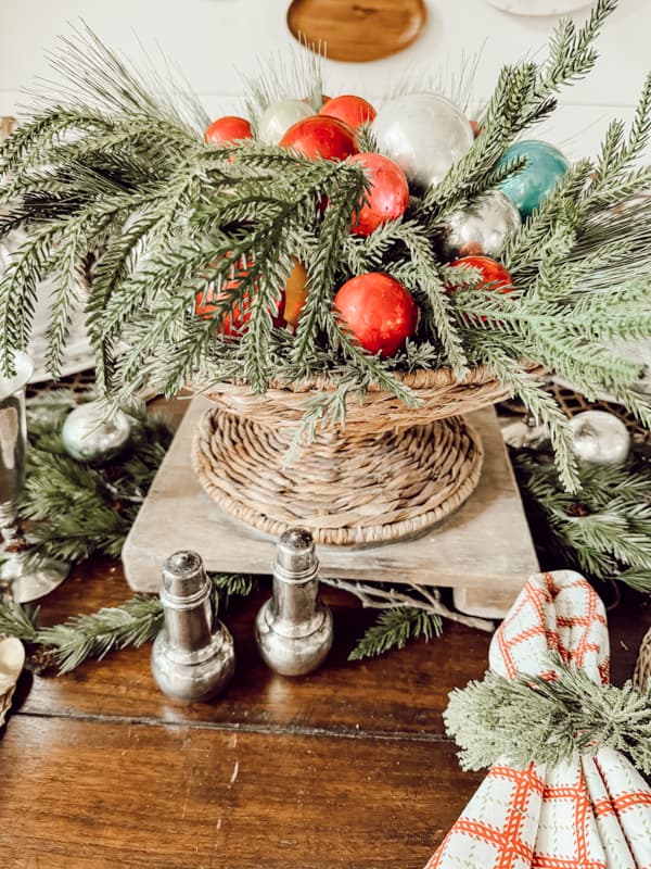 Christmas Table Centerpiece with a thrifted basket filled with greenery and colorful Glass Christmas ornaments.  