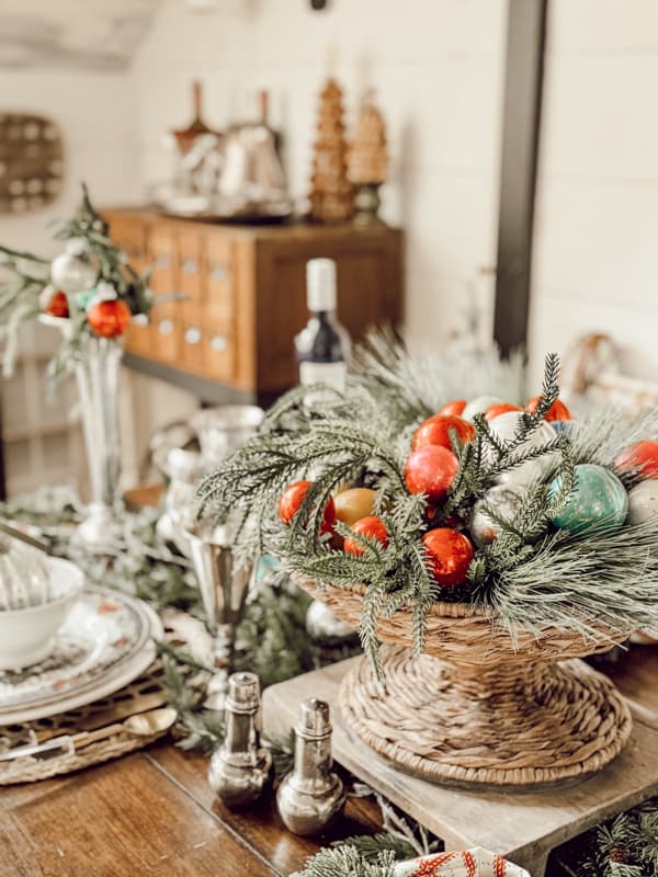 Basket centerpiece filled with greenery and vintage glass Christmas ornaments.