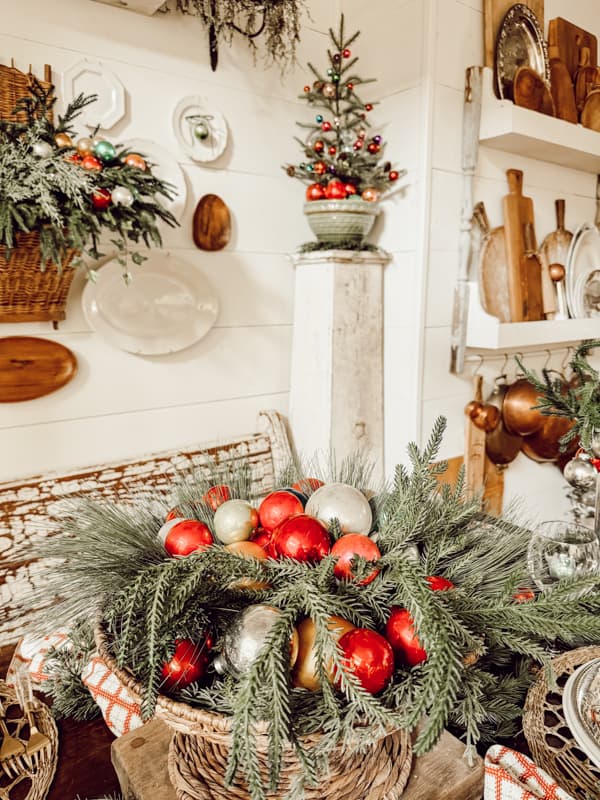 Christmas Table Centerpiece with a thrifted basket filled with greenery and colorful Glass Christmas ornaments.  