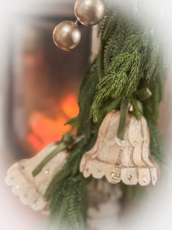 DIY Christmas Bells with old book pages on greenery mantel garland.  