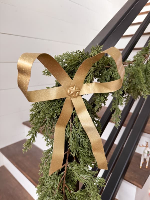 Metal Christmas bow attached to garland on banister