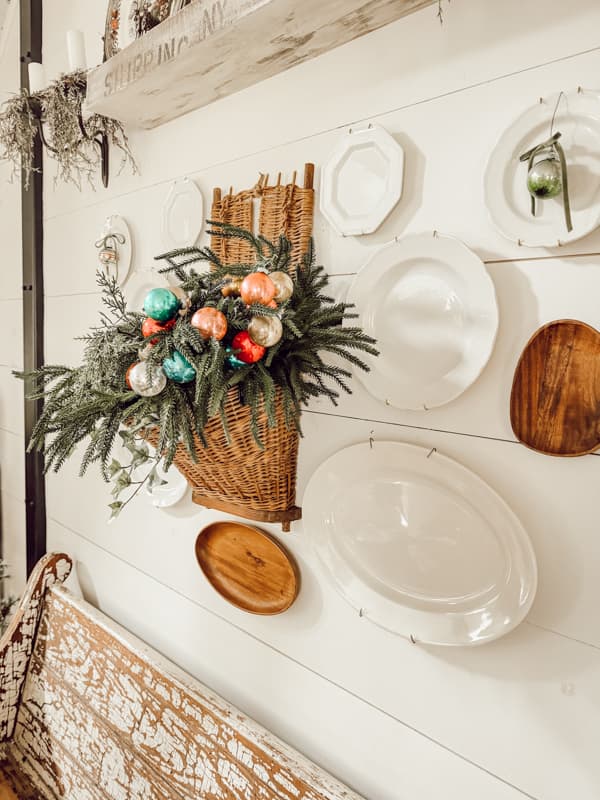 Retro Christmas Decor with European Wall Basket filled with vintage shiny brite ornaments and white ironstone plates on wall.  