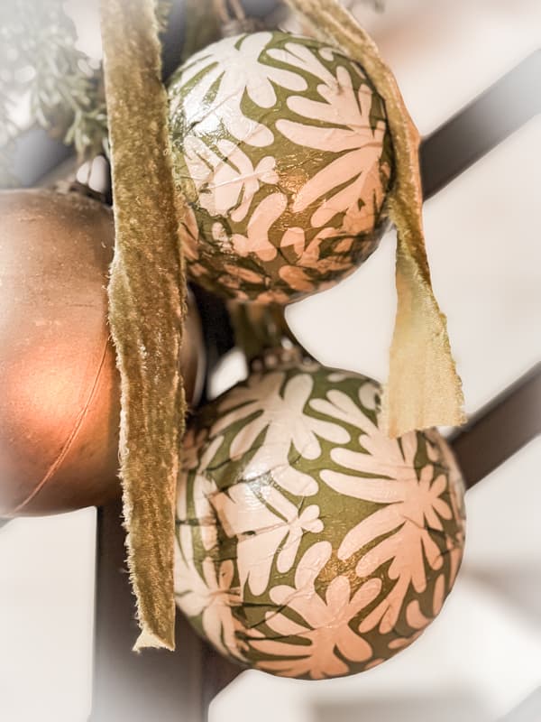 two napkin decoupage ornaments on staircase railing with gold ornament and green velvet ribbon