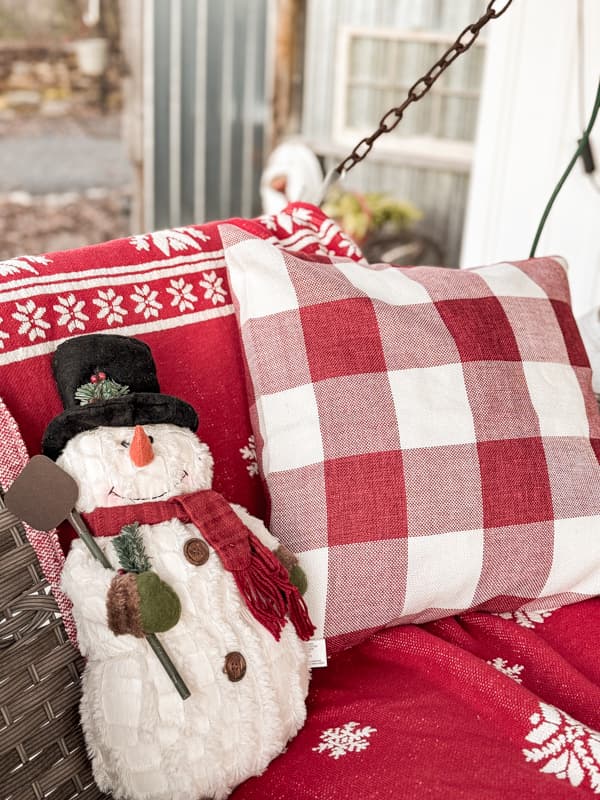 Snowman and red and white buffalo print pillows make the front porch swing extra cozy for Outdoor Christmas Decorations