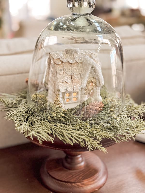 Tiny Christmas House with tea light under glass cloche with cedar candle ring on a large candleholder.