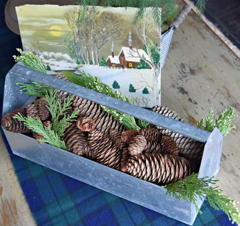 Old metal tool caddy with pinecones and vintage winter scene painting.  