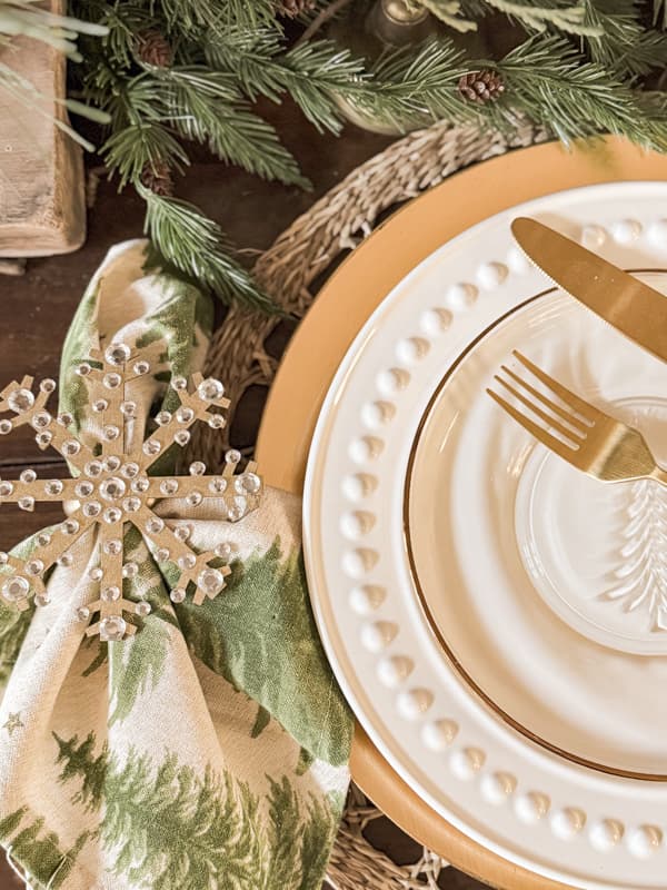 DIY Gold and rhinestone snowflake napkin ring beside place setting with Christmas tree napkin.