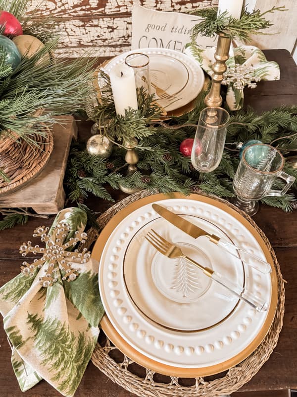 DIY Gold and rhinestone snowflake napkin ring beside place setting with Christmas tree napkin and Gold rimmed tableware.