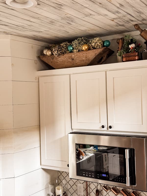 Christmas ornaments mixed with dried hydrangeas in dough bowl over kitchen cabinets.  